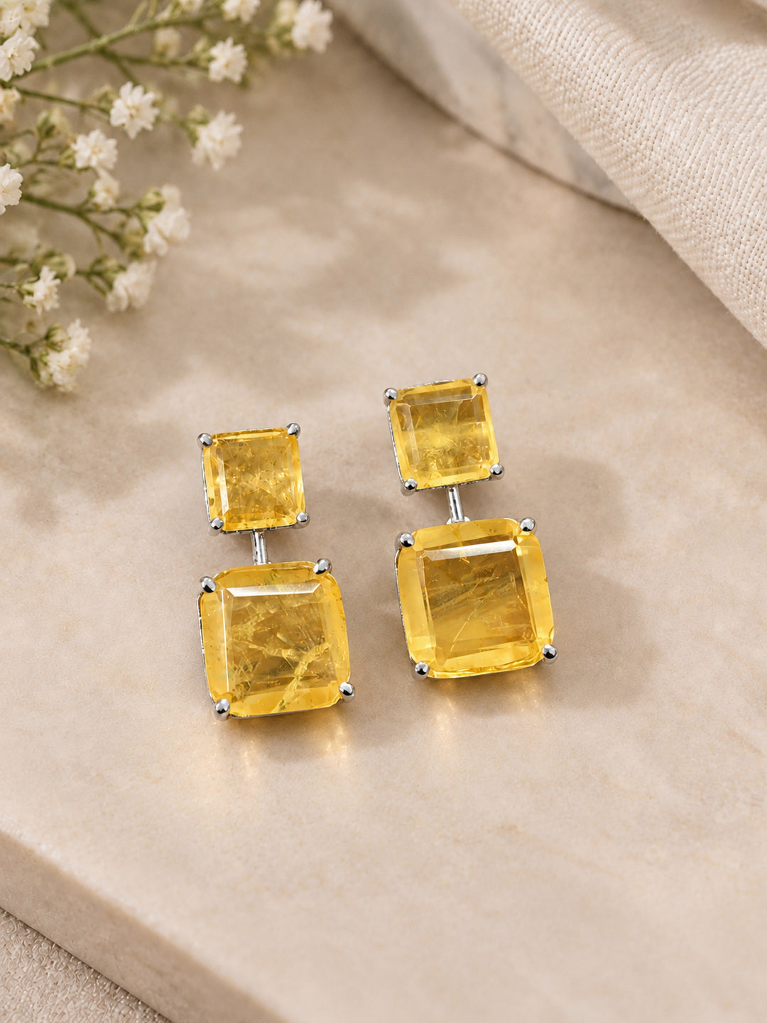 Close-up of citrine-yellow emerald-cut drop earrings with silver prong setting