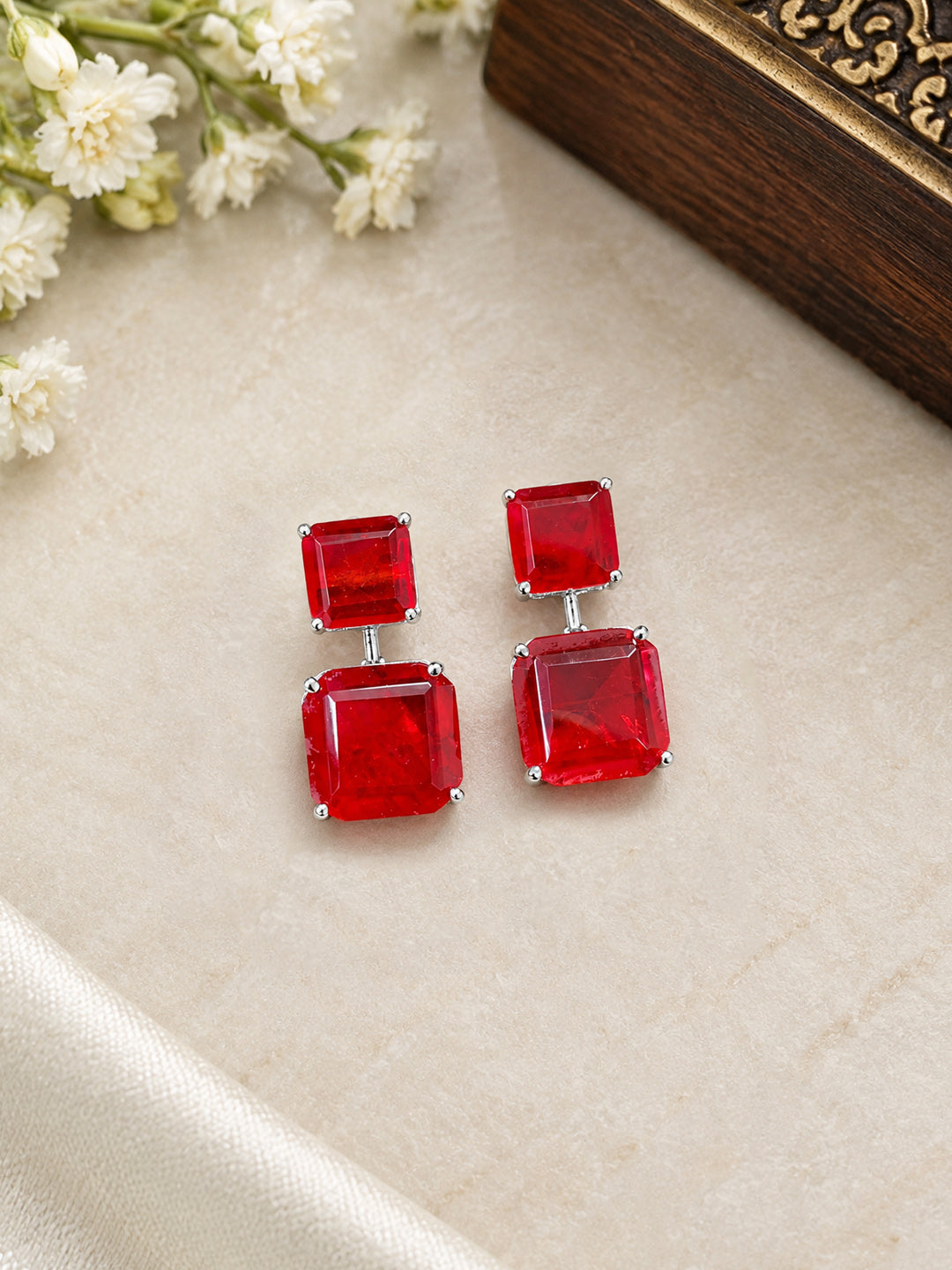 Close-up of ruby-red emerald-cut drop earrings with silver prong setting