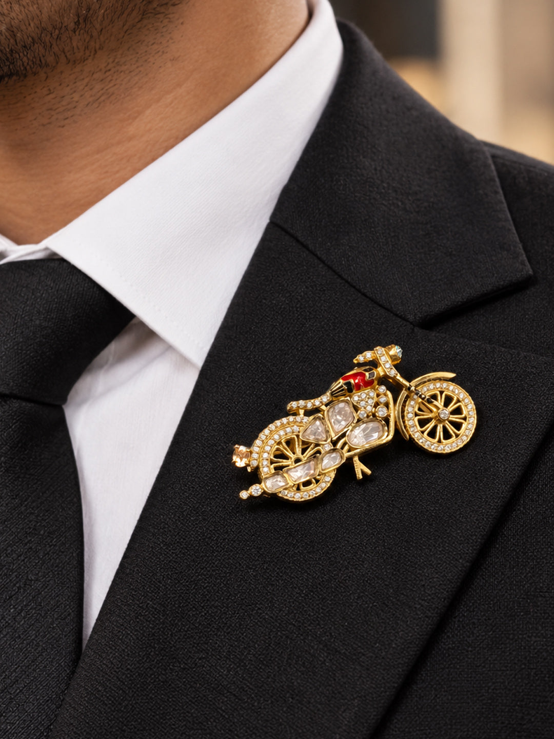 Close-up of gold motorcycle pin with kundan-style stones and detailed wheel design
