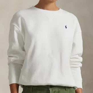 Person wearing a white sweatshirt with a logo and green pants against a beige background